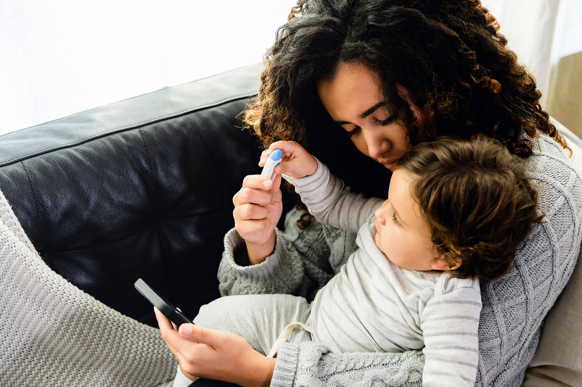 a woman and a baby sitting on a couch indoors looking at a cell phone