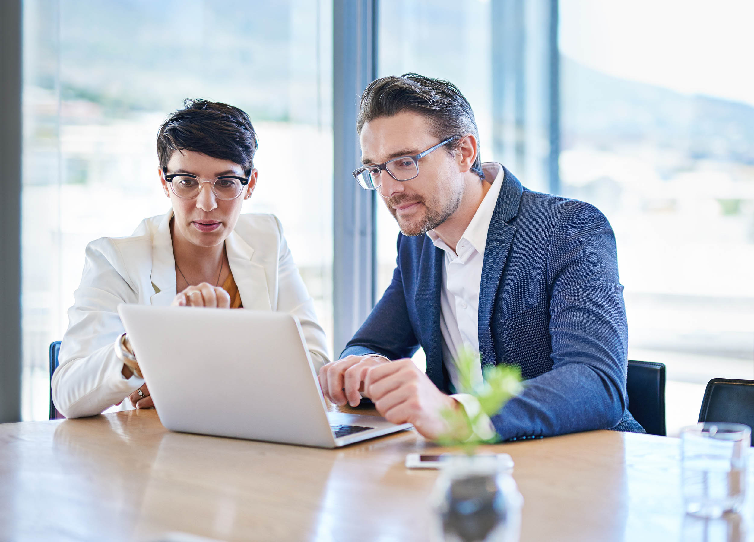 two business professionals in suits collaborating over a laptop
